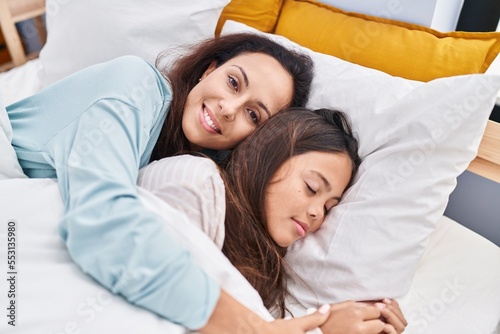 Woman and girl mother and daughter hugging each other lying on bed at bedroom