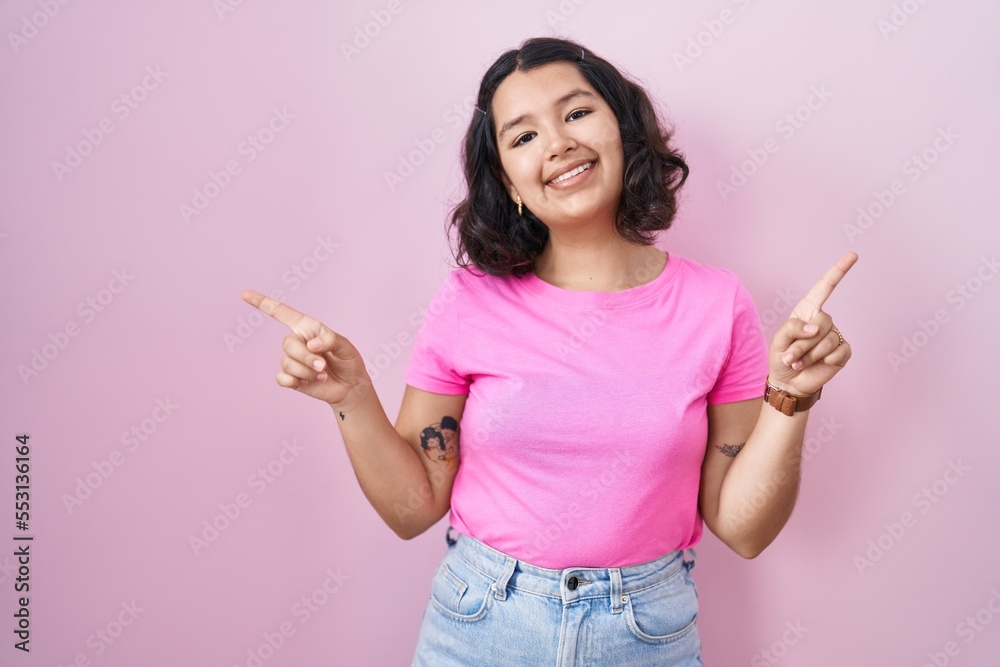 Young hispanic woman standing over pink background smiling confident pointing with fingers to different directions. copy space for advertisement Young hispanic woman standing over pink background smiling confident pointing with fingers to different directions. copy space for advertisement