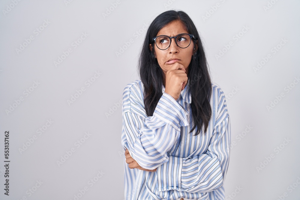 Young hispanic woman wearing glasses thinking worried about a question, concerned and nervous with hand on chin