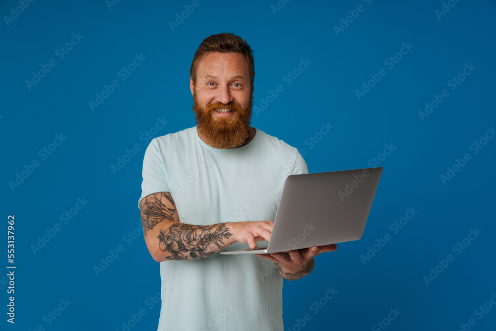 Ginger excited man with tattoo smiling and working with laptop Ginger excited man with tattoo smiling and working with laptop