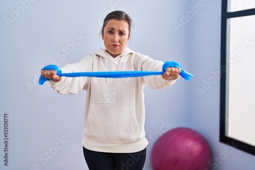 Middle age hispanic woman training arm resistance with elastic arm bands depressed and worry for distress, crying angry and afraid. sad expression.