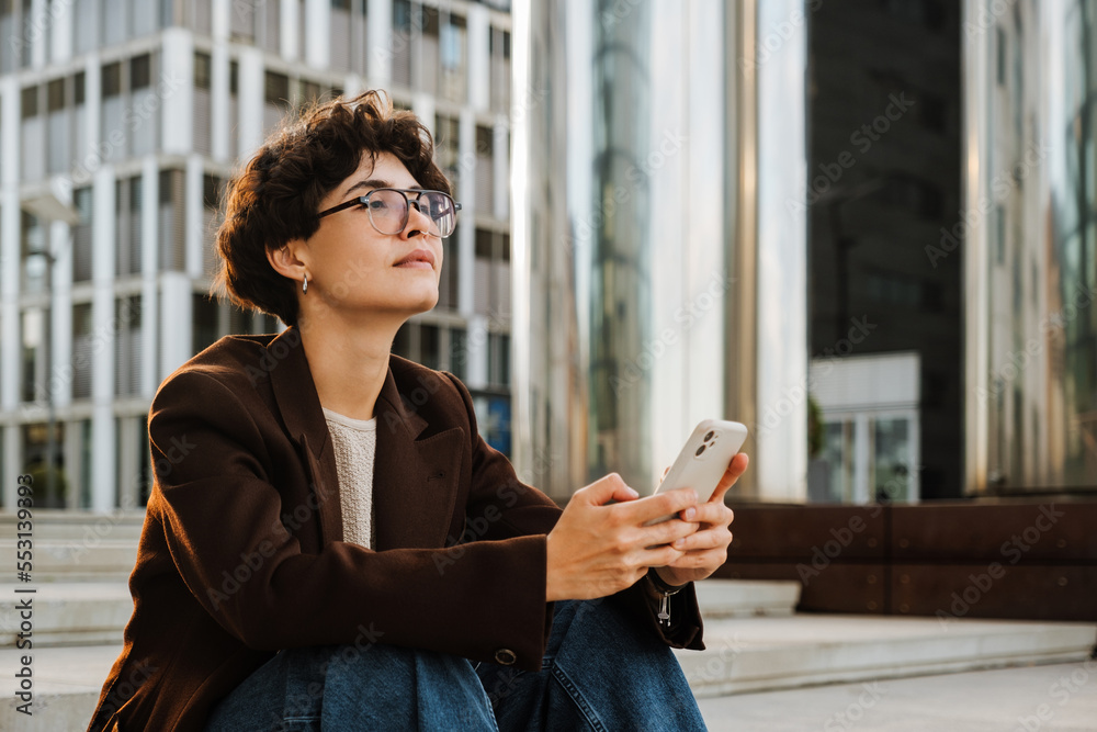 European woman using cellphone while sitting on stairs outdoors European woman using cellphone while sitting on stairs outdoors