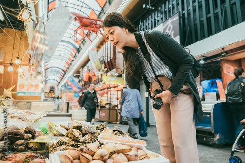 asian girl backpacker looking at fresh raw shellfish and thinking what to buy while shopping at a local seafood stall in kuromon ichiba market in Osaka japan photo