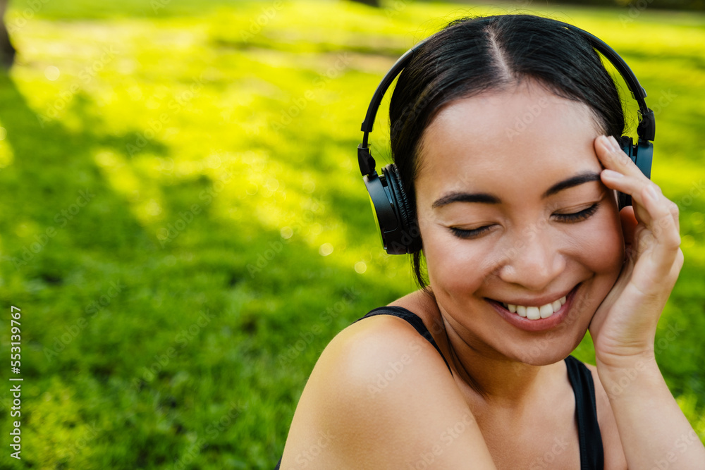 Young asian woman with headphones smiling during workout in park Young asian woman with headphones smiling during workout in park