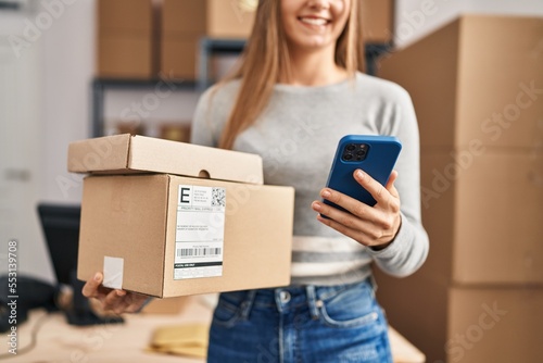 Obraz na płótnie Young blonde woman ecommerce business worker using smartphone holding packages a