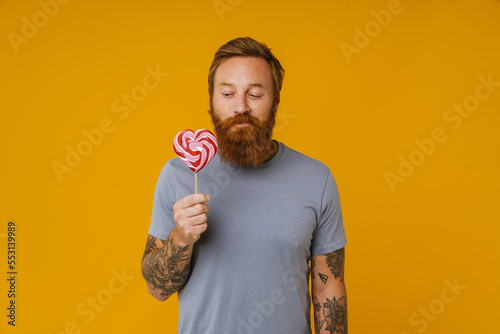 Bearded man holding lollipop while standing isolated over background