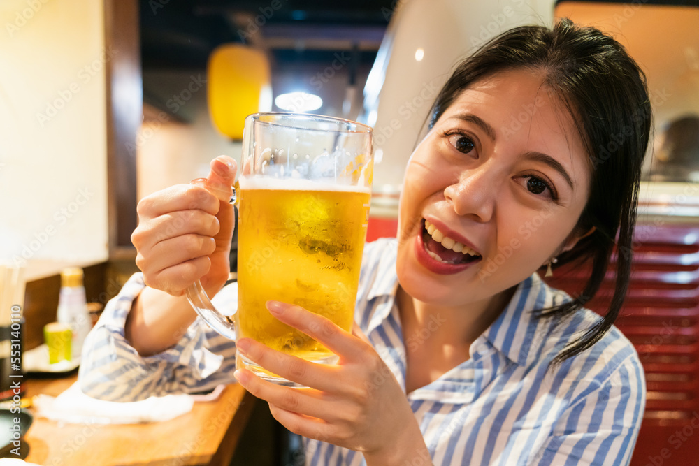 happy asian woman customer holding a glass mug of cold beer and smiling at camera while enjoying supper in a cozy izakaya Japanese bar in shinsekai new world Osaka japan happy asian woman customer holding a glass mug of cold beer and smiling at camera while enjoying supper in a cozy izakaya Japanese bar in shinsekai new world Osaka japan