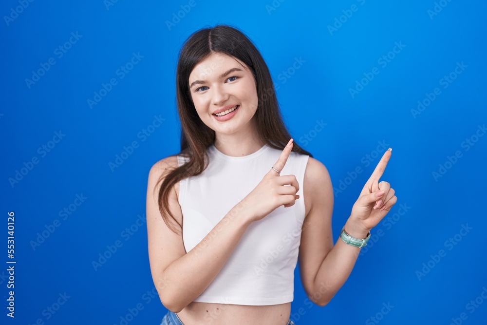 Young caucasian woman standing over blue background smiling and looking at the camera pointing with two hands and fingers to the side. Young caucasian woman standing over blue background smiling and looking at the camera pointing with two hands and fingers to the side.