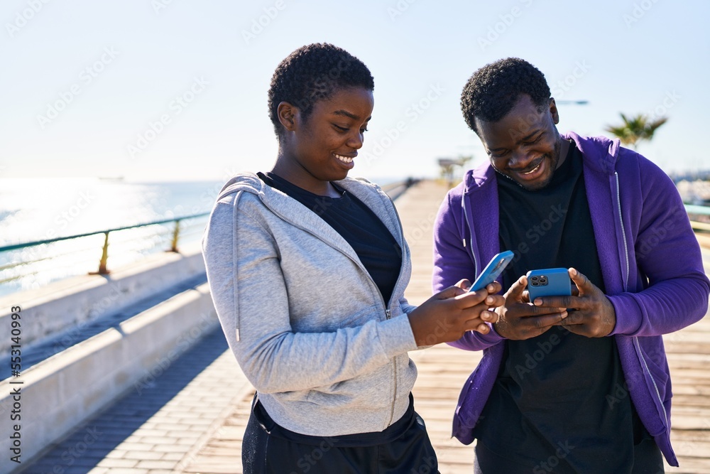 Man and woman couple wearing sportswear using smartphone at seaside