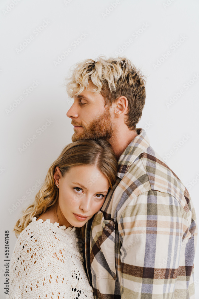 Young beautiful couple hugging while standing isolated over white wall Young beautiful couple hugging while standing isolated over white wall