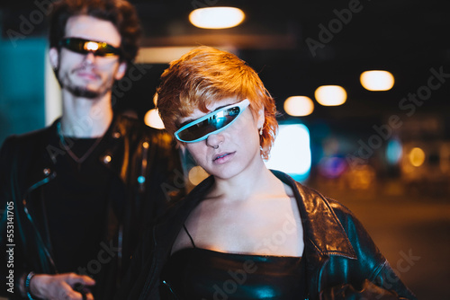 Young woman wearing smart glasses with boyfriend in background at illuminated underpass photo