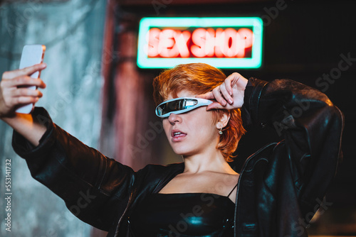 Young woman with smart glasses taking selfie through smart phone outside sex shop