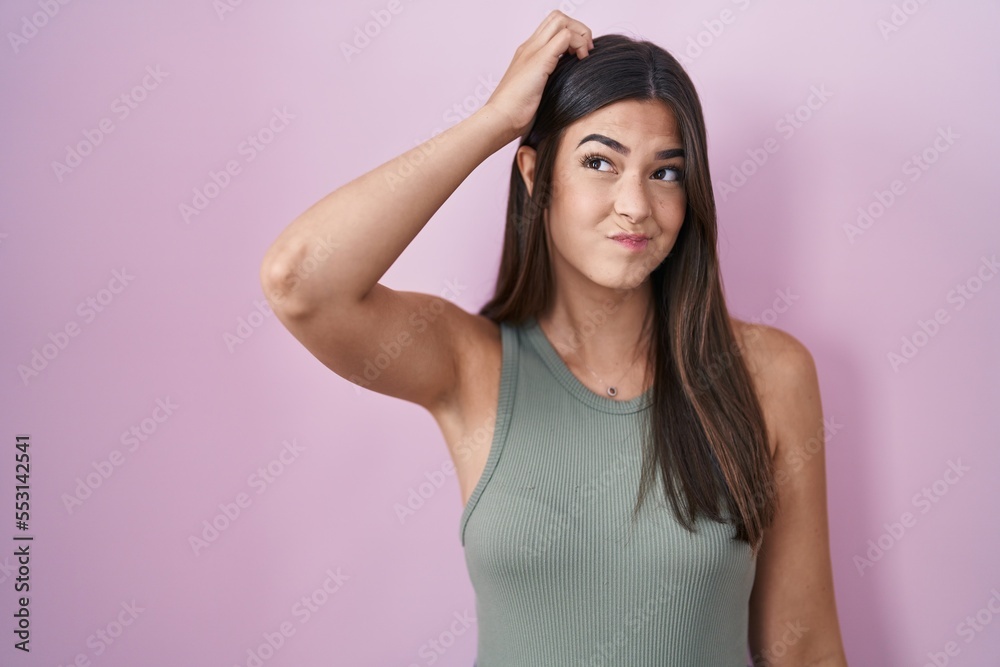 Hispanic woman standing over pink background confuse and wonder about question. uncertain with doubt, thinking with hand on head. pensive concept. Hispanic woman standing over pink background confuse and wonder about question. uncertain with doubt, thinking with hand on head. pensive concept.
