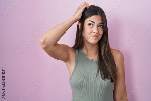 Hispanic woman standing over pink background confuse and wonder about question. uncertain with doubt, thinking with hand on head. pensive concept.
