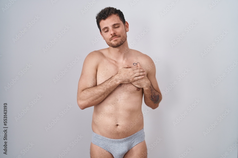 Young hispanic man standing shirtless wearing underware smiling with hands on chest with closed eyes and grateful gesture on face. health concept.