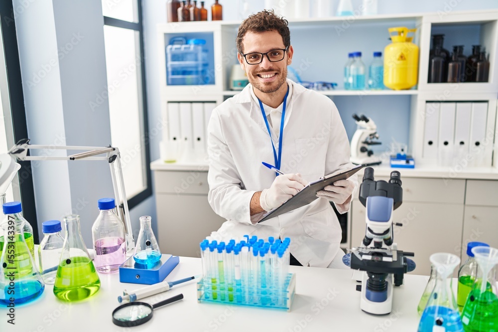 Young hispanic man scientist looking test tubes write on document at laboratory Young hispanic man scientist looking test tubes write on document at laboratory