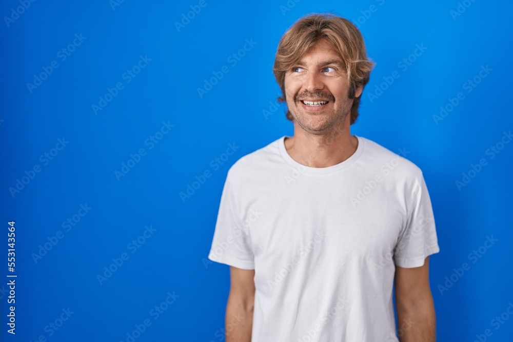 Middle age man standing over blue background smiling looking to the side and staring away thinking. Middle age man standing over blue background smiling looking to the side and staring away thinking.