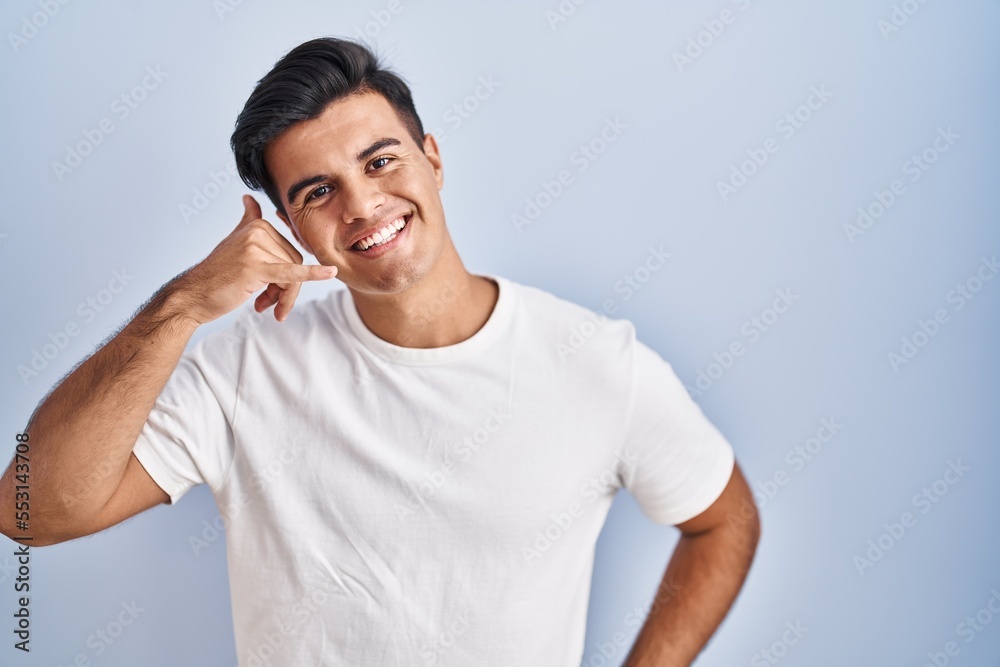 Hispanic man standing over blue background smiling doing phone gesture with hand and fingers like talking on the telephone. communicating concepts. Hispanic man standing over blue background smiling doing phone gesture with hand and fingers like talking on the telephone. communicating concepts.