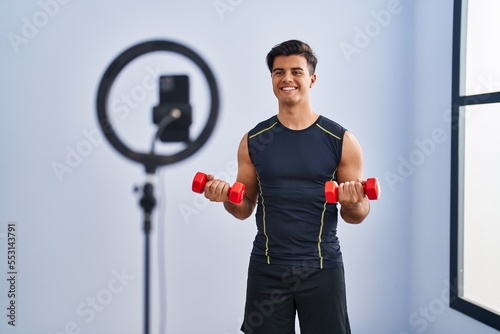Hispanic man recording training tutorial at the gym smiling with a happy and cool smile on face. showing teeth.