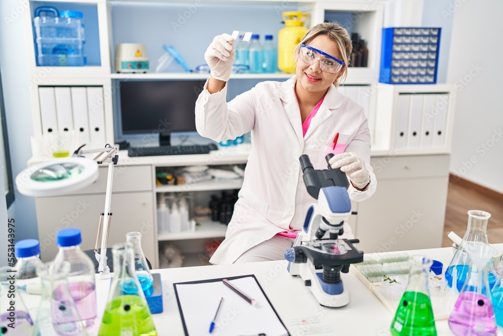 Young hispanic woman wearing scientist uniform using microscope at laboratory Young hispanic woman wearing scientist uniform using microscope at laboratory