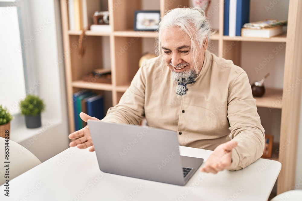 Middle age grey-haired man having video call sitting on table at home Middle age grey-haired man having video call sitting on table at home