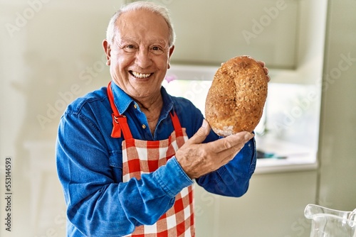 Senior man smiling confident holding wholemeal bread at kitchen photo