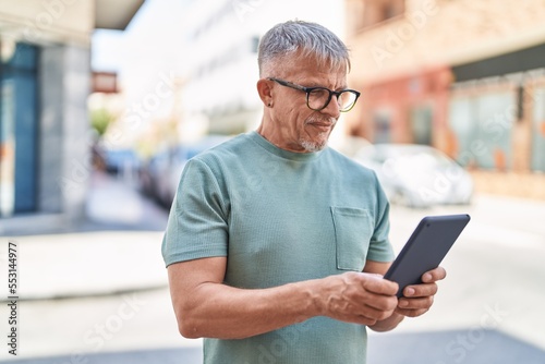 Middle age grey-haired man smiling confident using touchpad at street
