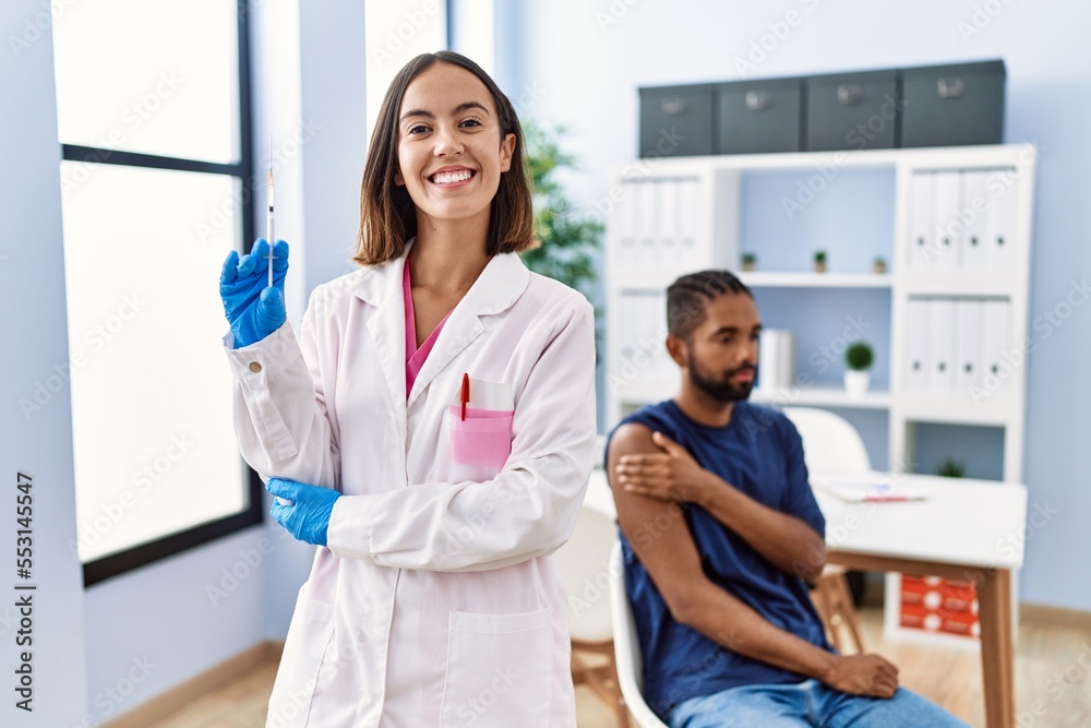 Fototapeta premium Young doctor woman holding vaccine showing syringe looking positive and happy standing and smiling with a confident smile showing teeth