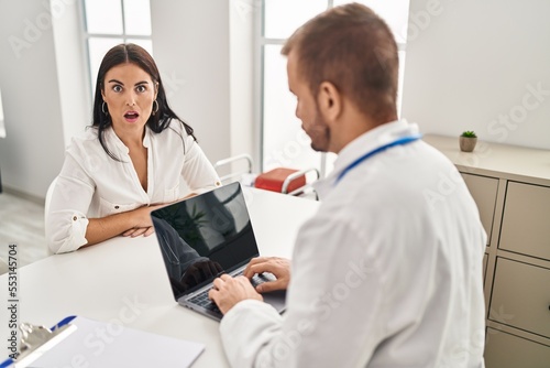 Young hispanic woman at the doctor scared and amazed with open mouth for surprise, disbelief face