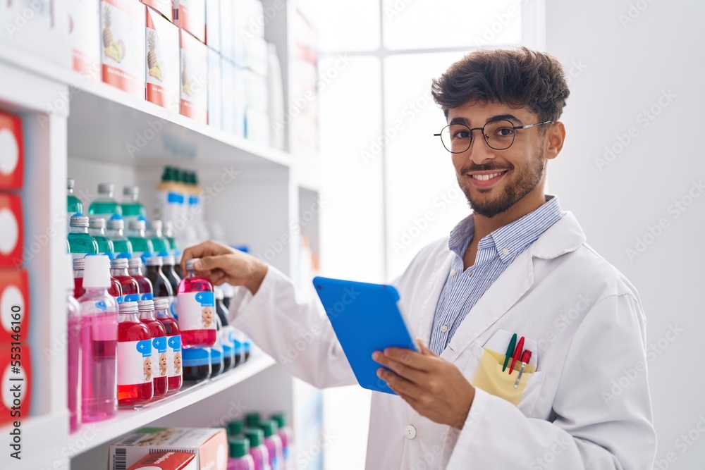 Young arab man pharmacist using touchpad holding medicine bottle at pharmacy