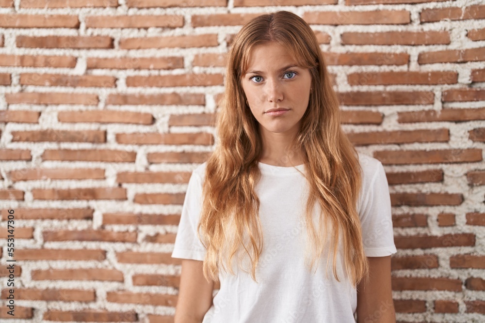 Young caucasian woman standing over bricks wall relaxed with serious expression on face. simple and natural looking at the camera. Young caucasian woman standing over bricks wall relaxed with serious expression on face. simple and natural looking at the camera.