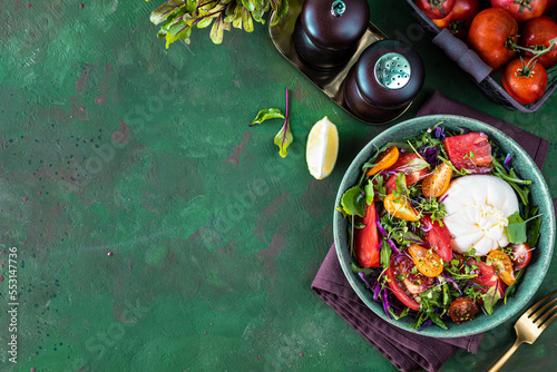 Salad with tomatoes, arugula, Burrata cheese and microgreens on a green stone background, top view. copy space