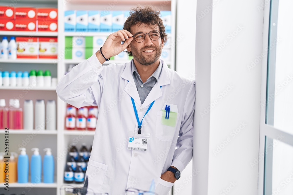 Young hispanic man pharmacist smiling confident standing at pharmacy