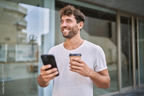 Young hispanic man using smartphone drinking coffee at street