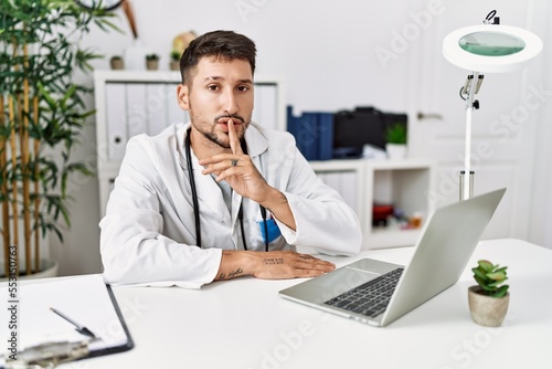 Young doctor working at the clinic using computer laptop asking to be quiet with finger on lips. silence and secret concept.