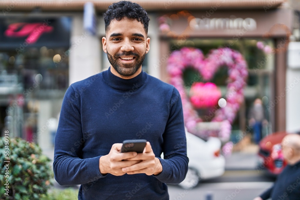 Young hispanic man smiling confident using smartphone at street