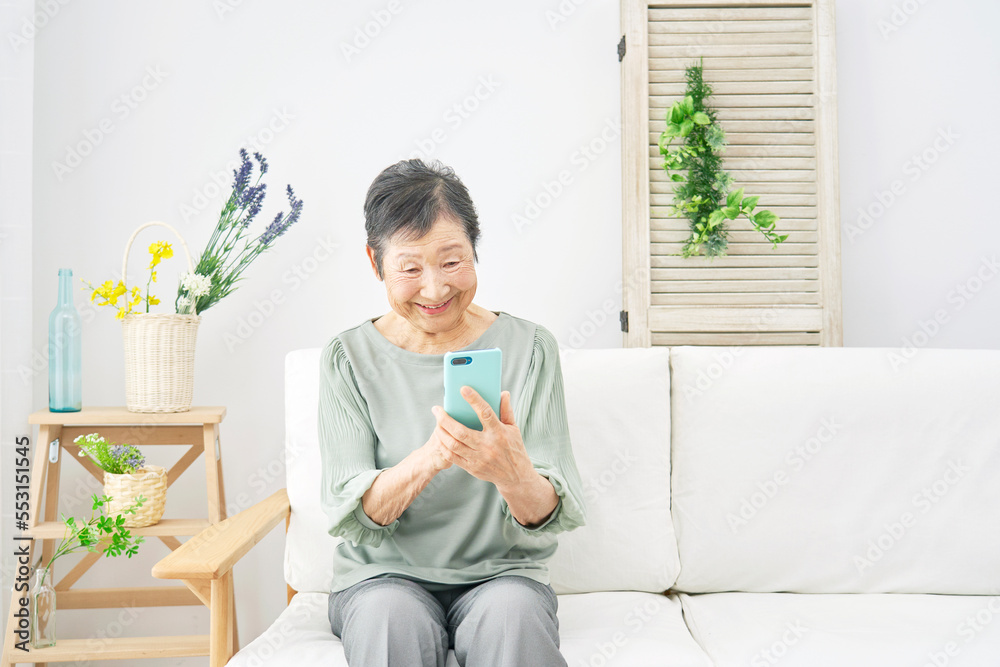 家で笑顔でスマホを使う高齢者女性 家で笑顔でスマホを使う高齢者女性