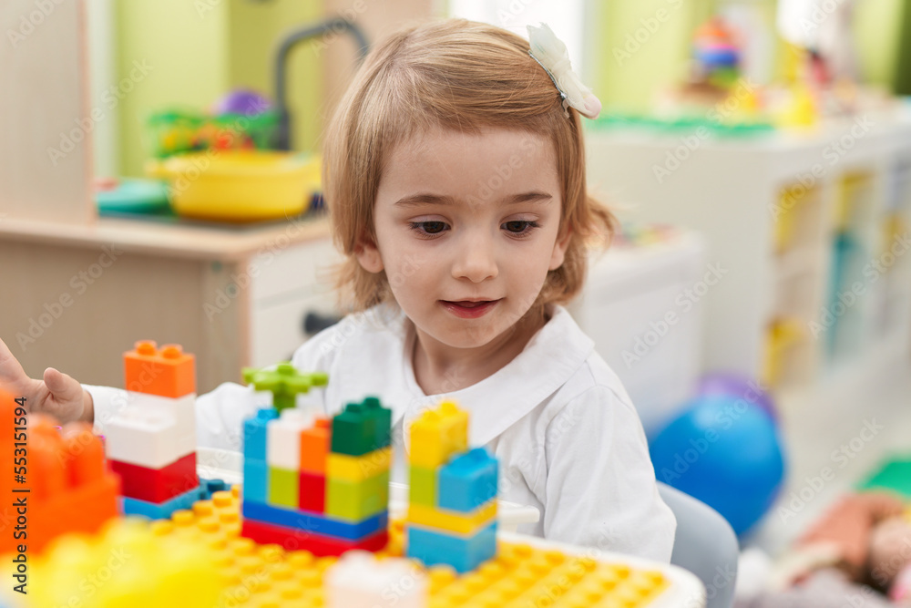 Adorable caucasian girl playing with construction blocks sitting on table at kindergarten Adorable caucasian girl playing with construction blocks sitting on table at kindergarten