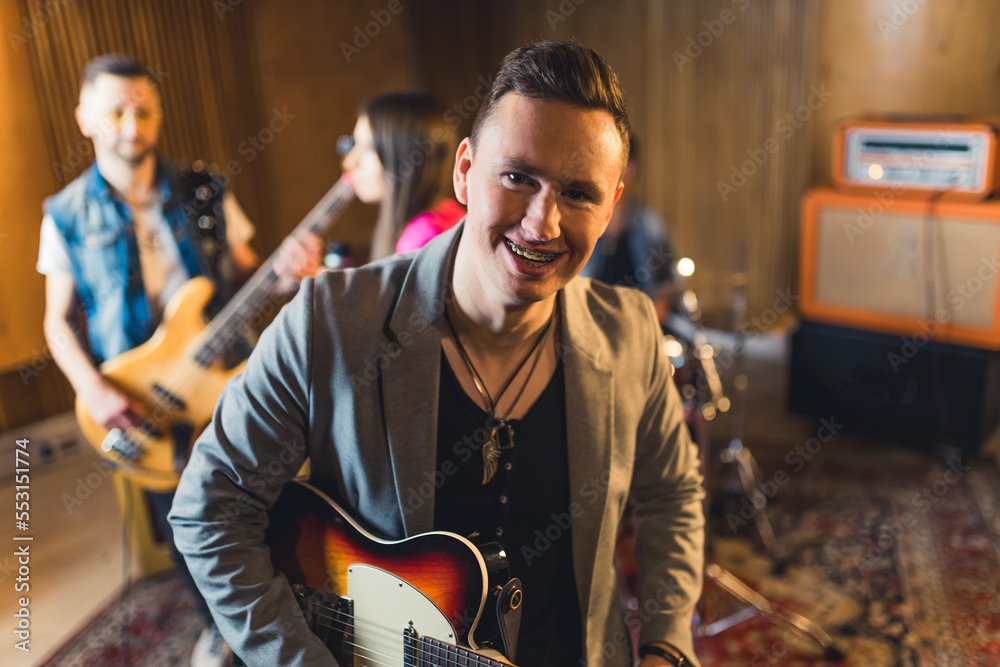 Caucasian adult man holding electric guitar, smiling, and looking at camera. Garage studio interior. Rock band concept. High quality photo