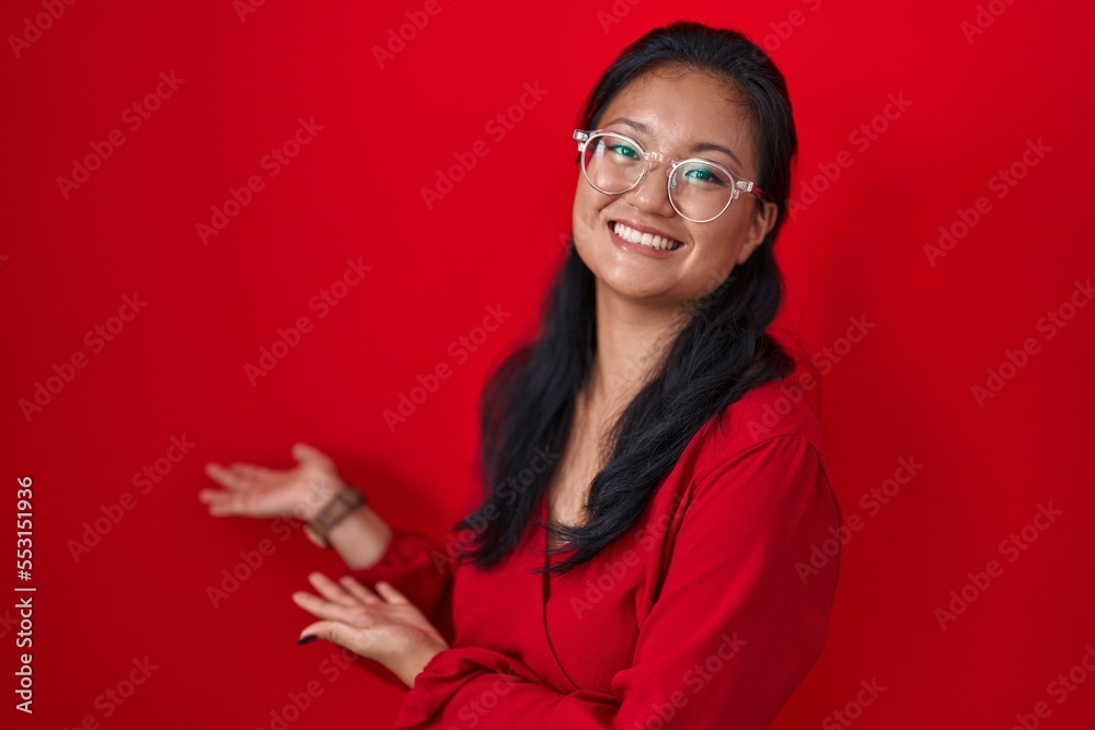 Asian young woman standing over red background inviting to enter smiling natural with open hand