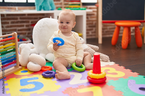 Adorable caucasian baby holding hoop toy sitting on floor at kindergarten