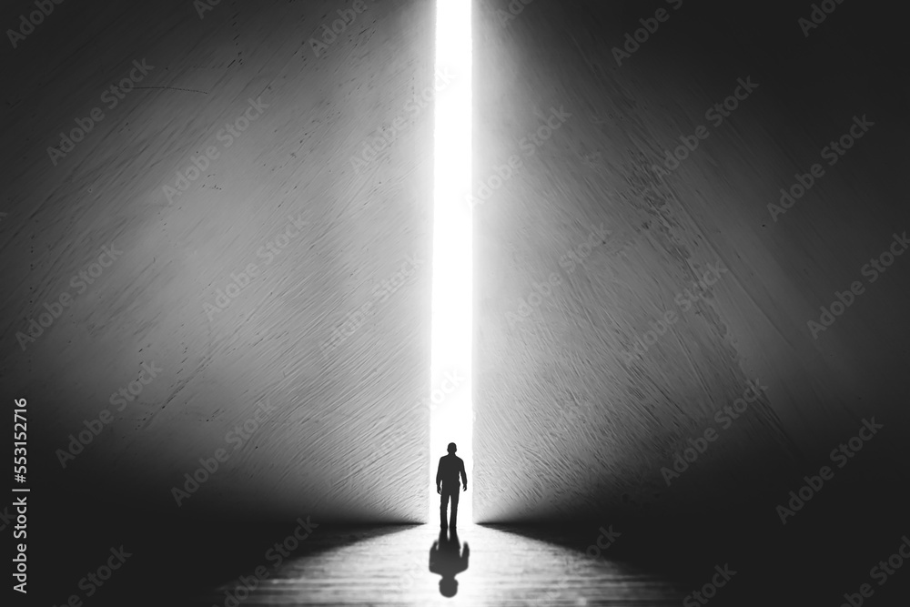 The silhouette of a man walking towards a bright light in the opened ...