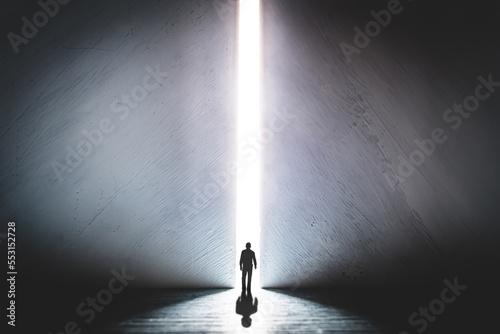 Fototapeta Naklejka Na Ścianę i Meble -  The silhouette of a man walking towards a bright light in the opened huge wall. A light in the end of a tunnel. The concept of success, freedom of choice, open mind, meditation.