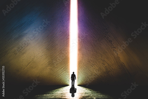 The silhouette of a man walking towards a bright light in the opened huge wall. A light in the end of a tunnel. The concept of success, freedom of choice, open mind, meditation.