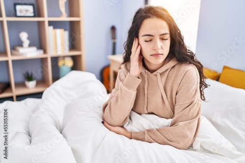 Young hispanic woman sitting on bed suffering for ear pain at bedroom