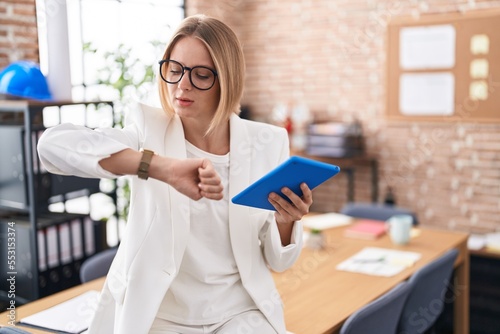 Young caucasian woman working at the office wearing glasses checking the time on wrist watch, relaxed and confident photo