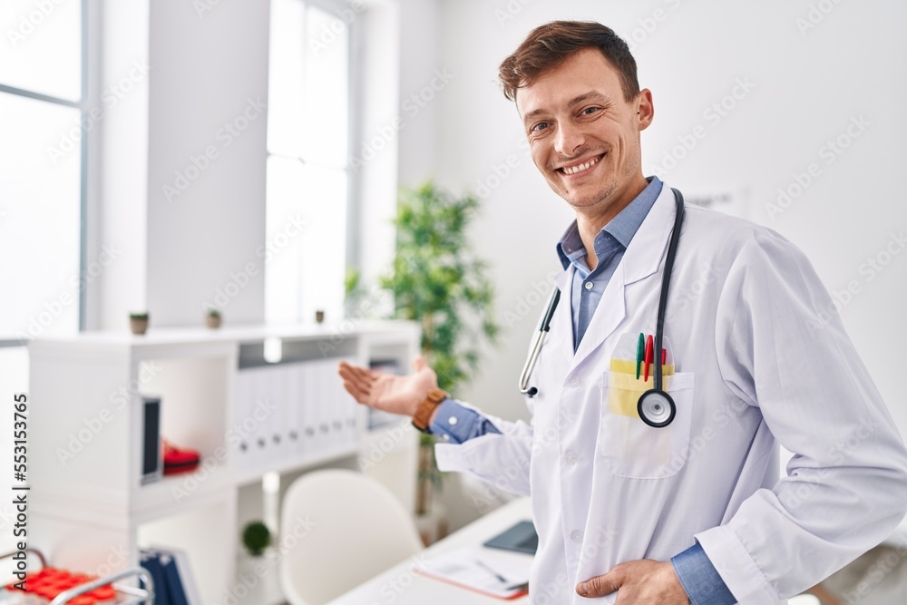 Young man doctor smiling confident standing with welcome gesture at clinic