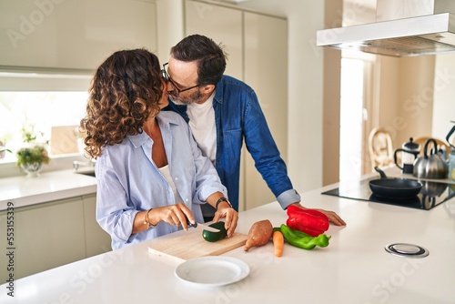 Middle age hispanic couple kissing and hugging each other cooking at kitchen