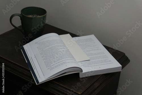 Open book and coffee cup on bedside table