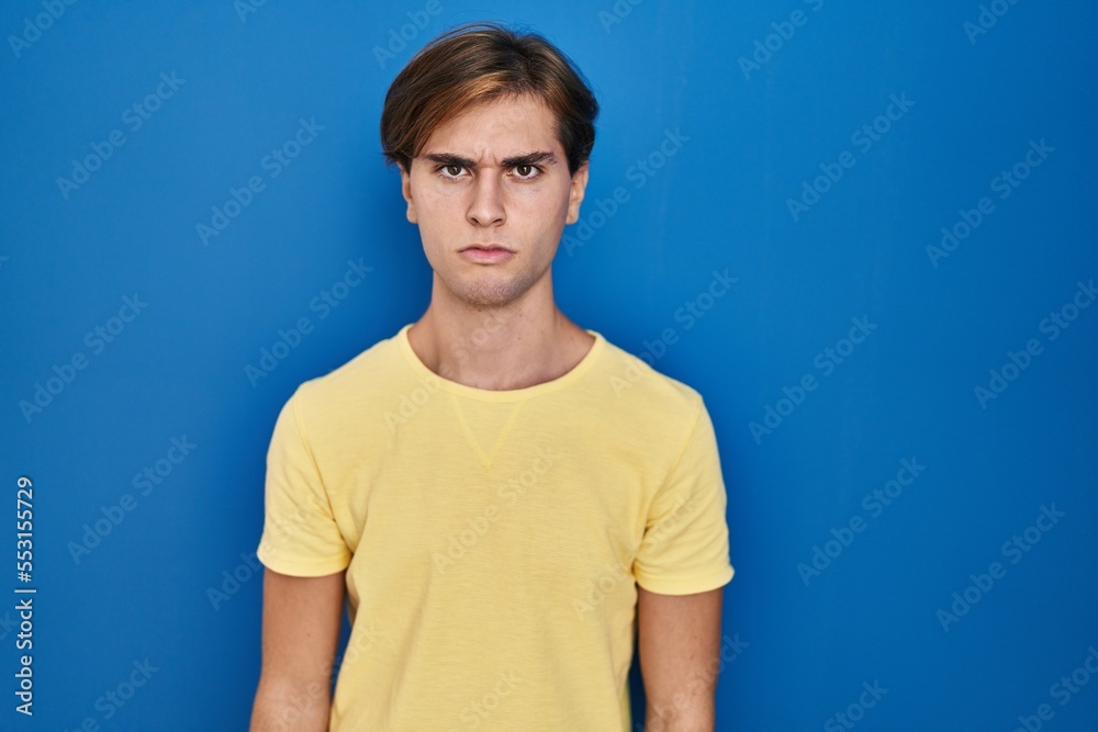 Young man standing over blue background skeptic and nervous, frowning upset because of problem. negative person.